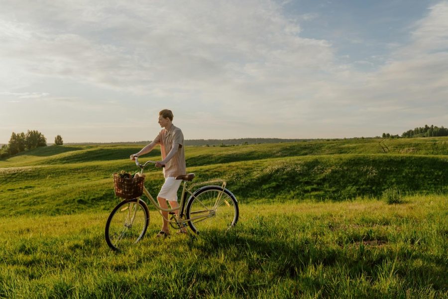 A man walking his bicycle through a lush green meadow on a sunny summer day.