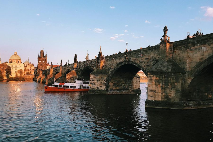 Scenic view of the Charles Bridge and iconic Prague landmarks during sunset with a boat on the Vltava River.